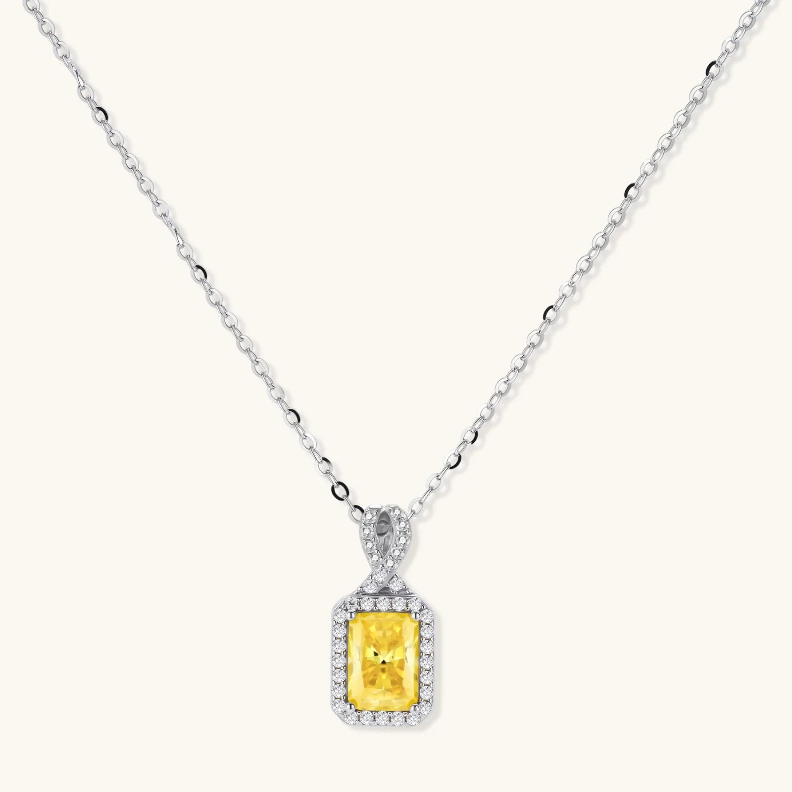 Rectangular yellow moissanite pendant in sterling silver halo setting on delicate chain against cream background.