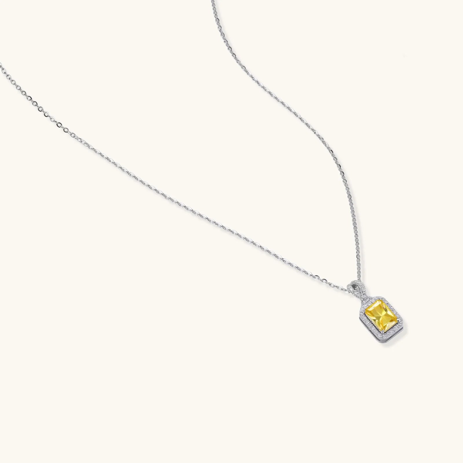 Rectangular yellow moissanite pendant in sterling silver halo setting on delicate chain against cream background.
