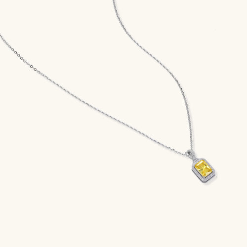 Rectangular yellow moissanite pendant in sterling silver halo setting on delicate chain against cream background.