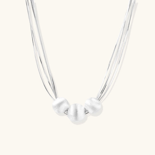 Sterling silver multi-strand necklace with three brushed round beads on cream background