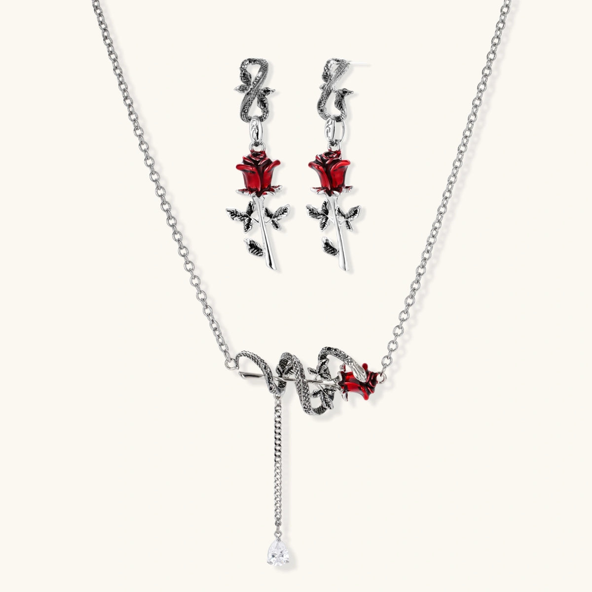 Gothic jewelry set with silver snake designs holding red enamel roses, featuring detailed leaf stems on cream background