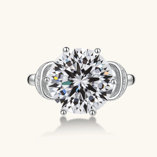 Sterling silver ring with 5ct round moissanite center stone and intricate bow design with pavé accents on white background.