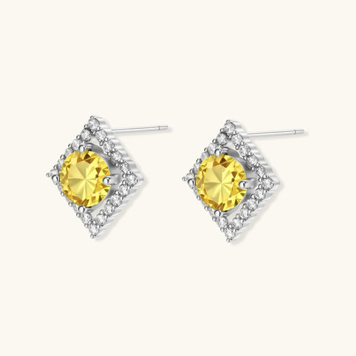 Close-up of diamond-shaped stud earrings with yellow moissanite centers and clear stone halos in sterling silver setting
