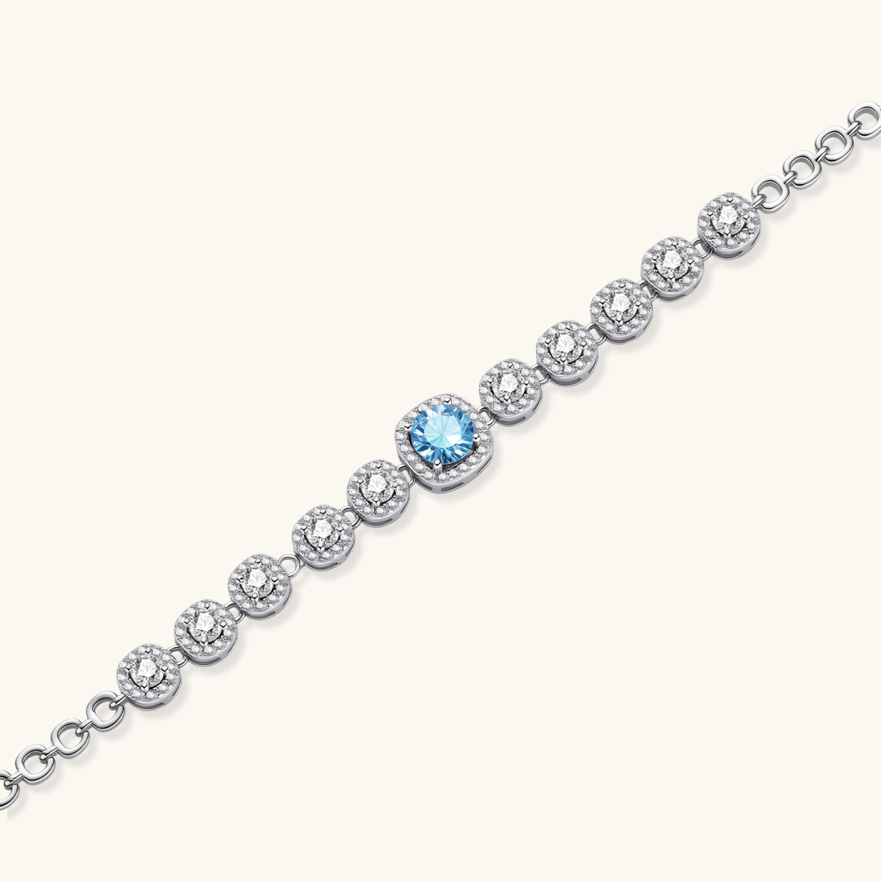 Sterling silver tennis bracelet with round halo-set moissanite stones and blue center stone on cream background.