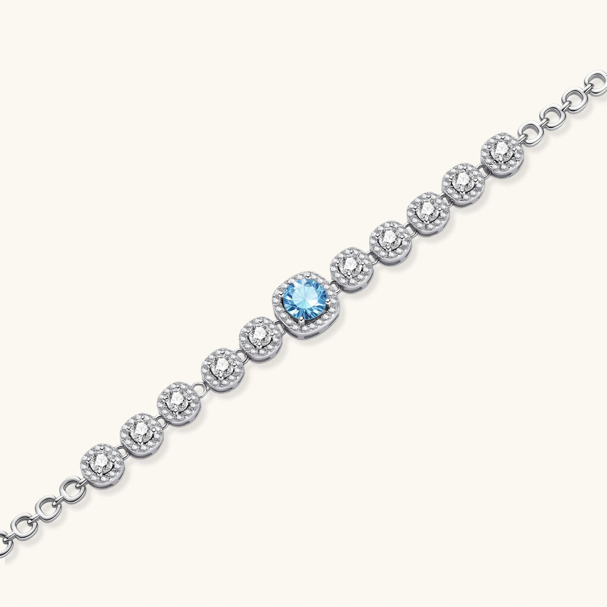 Sterling silver tennis bracelet with round halo-set moissanite stones and blue center stone on cream background.