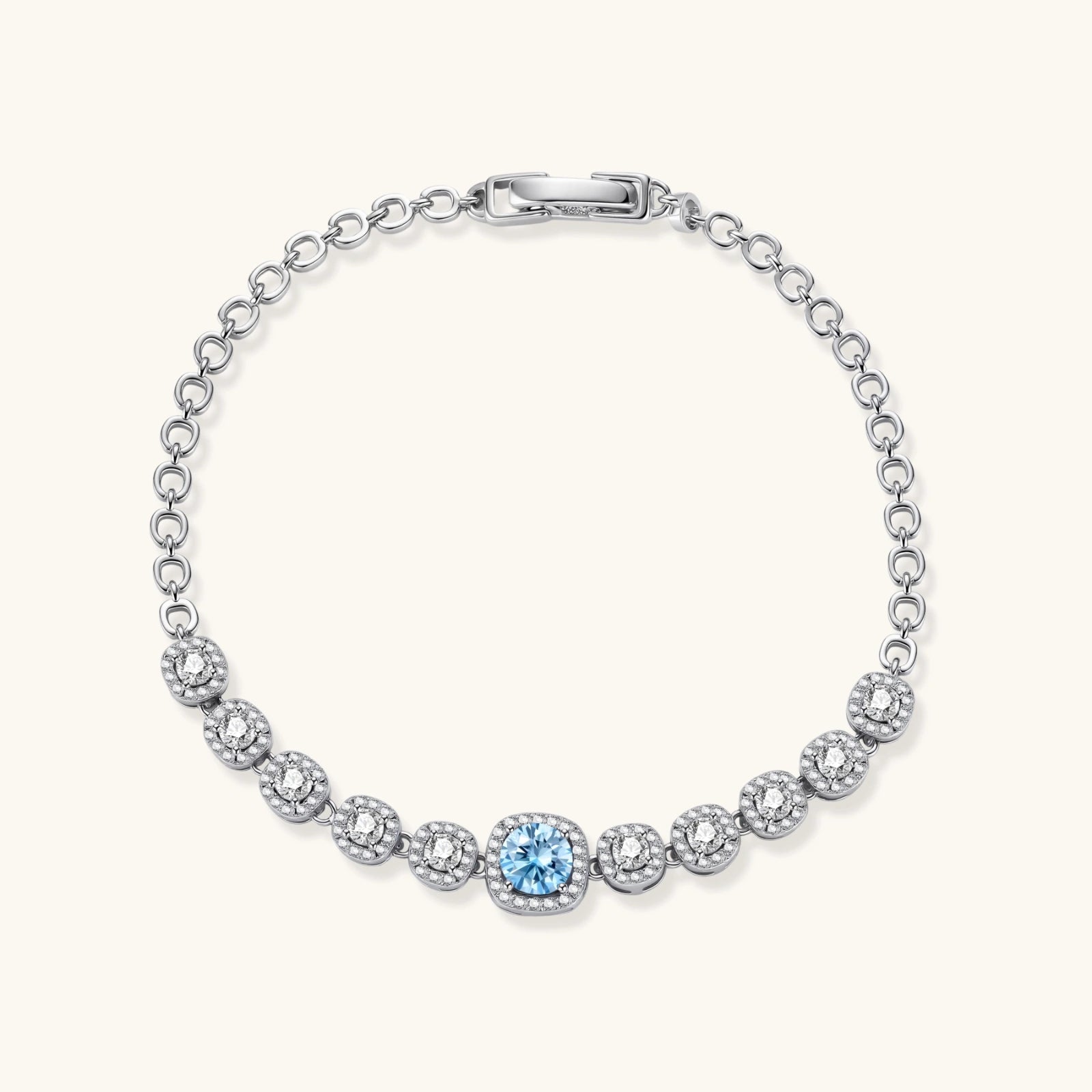 Sterling silver tennis bracelet with round halo-set moissanite stones and blue center stone on cream background.