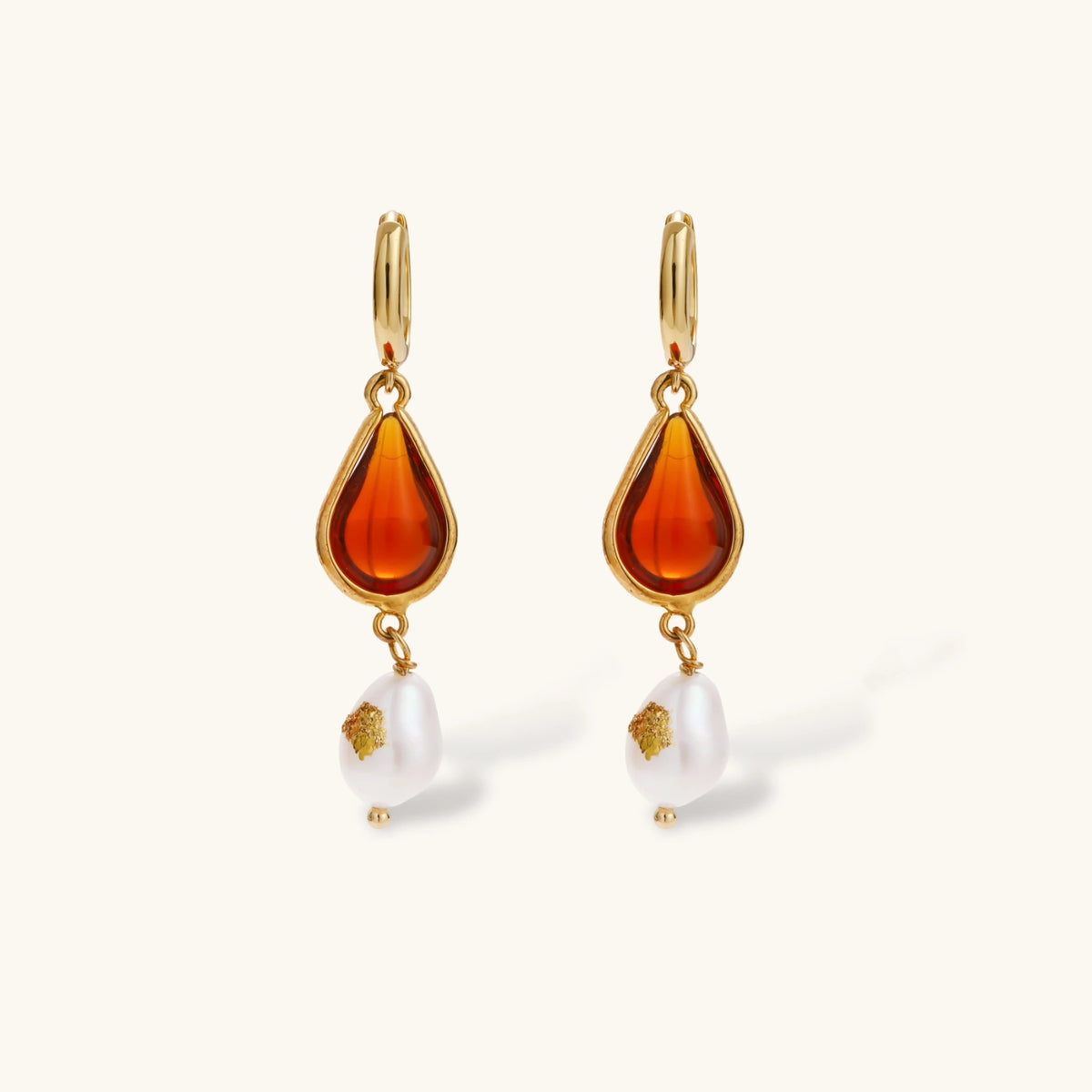 Gold-plated drop earrings featuring amber teardrops and white baroque pearls on light background.