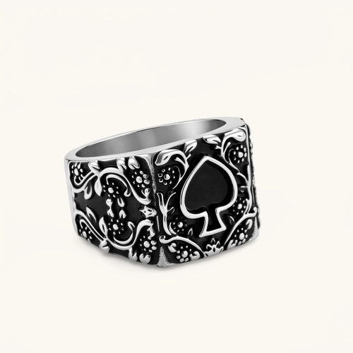 Silver-tone 316L stainless steel signet ring with black enamel spade motif and intricate floral scrollwork relief detail.