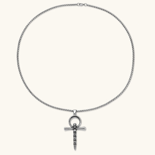 Silver stainless steel ankh pendant with skull motifs on vertical bar and textured ring top, on a box chain necklace.