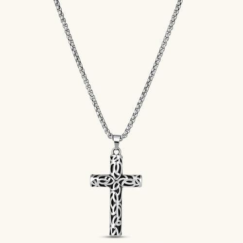 Silver stainless steel Celtic cross pendant with filigree vine pattern on a box chain, against a cream background.
