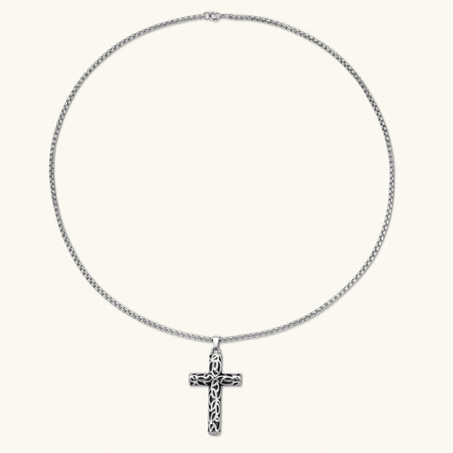Silver stainless steel Celtic cross pendant with filigree vine pattern on a box chain, against a cream background.