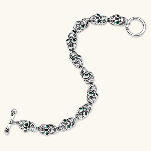 Silver stainless steel skull link bracelet with green crystal eye sockets and engraved detailing, toggle clasp closure.