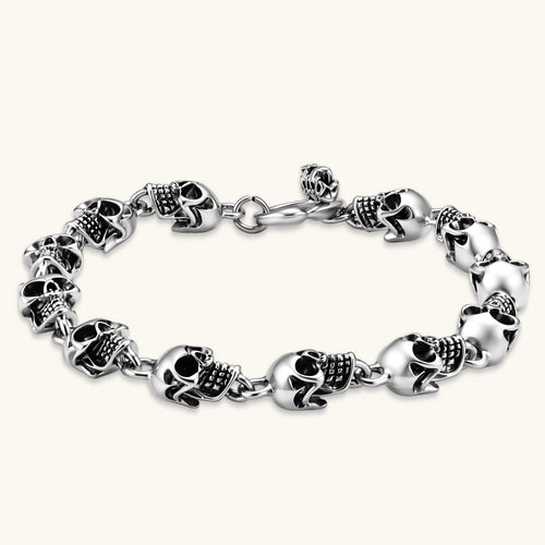 Silver stainless steel bracelet with linked 3D skull charms and a spring-ring clasp, oxidized black detailing, 225mm length.
