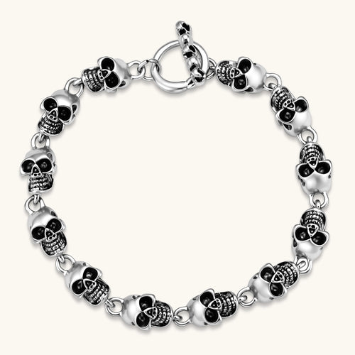 Silver stainless steel bracelet with linked 3D skull charms and a spring-ring clasp, oxidized black detailing, 225mm length.