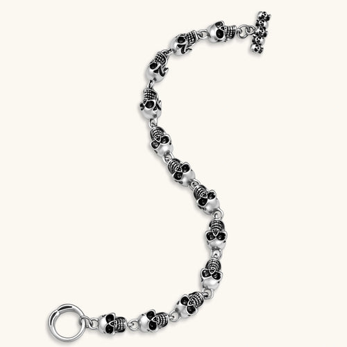Silver stainless steel bracelet with linked 3D skull charms and a spring-ring clasp, oxidized black detailing, 225mm length.