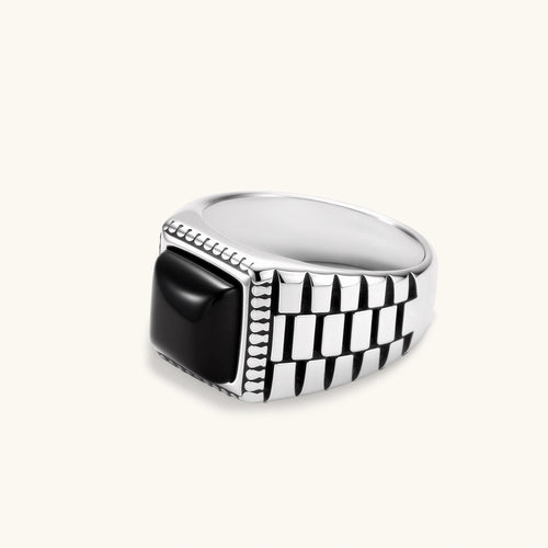 Silver stainless steel signet ring with checkered band texture, beaded border, and square black onyx cabochon stone center.